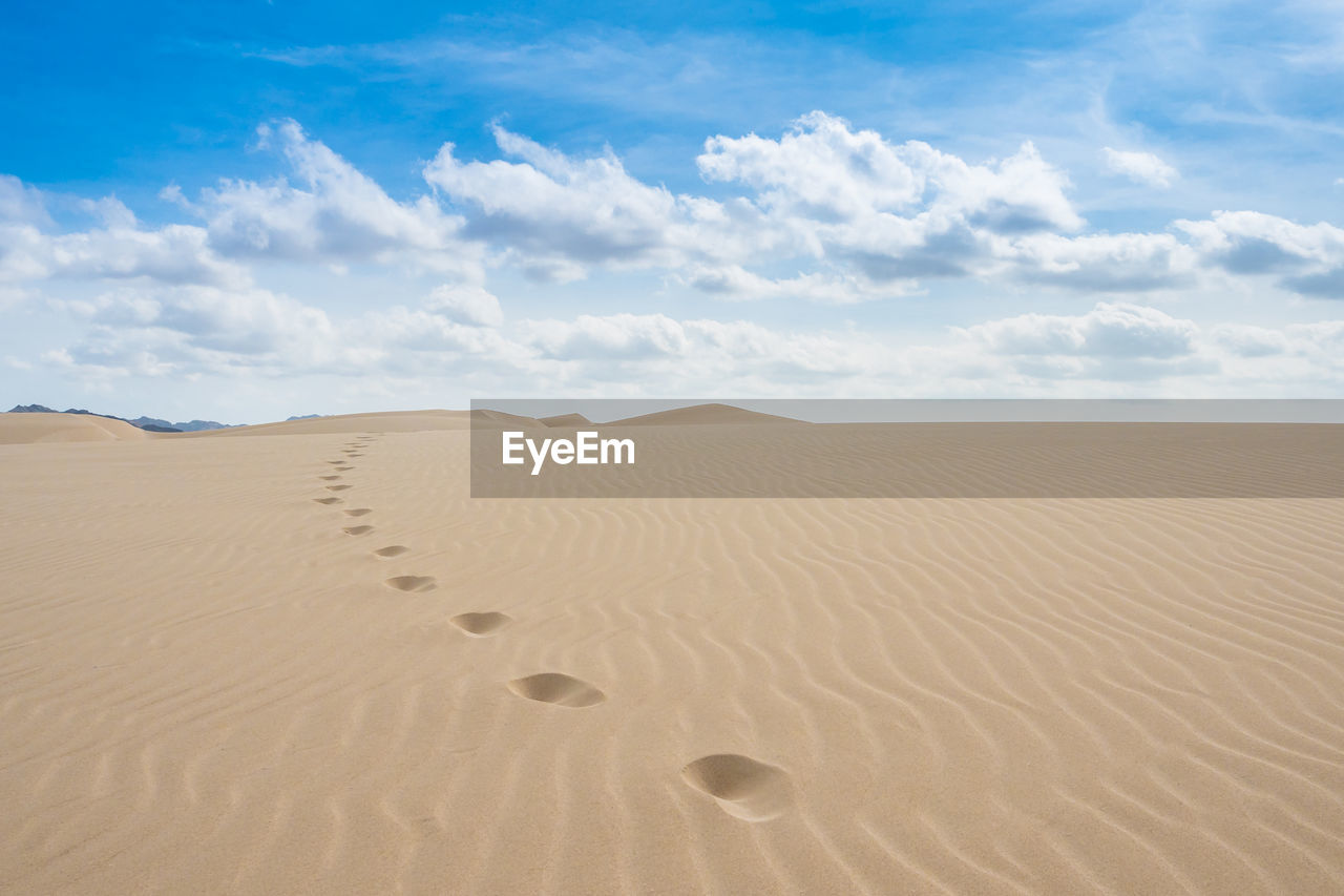 Footprints on sand in desert against sky