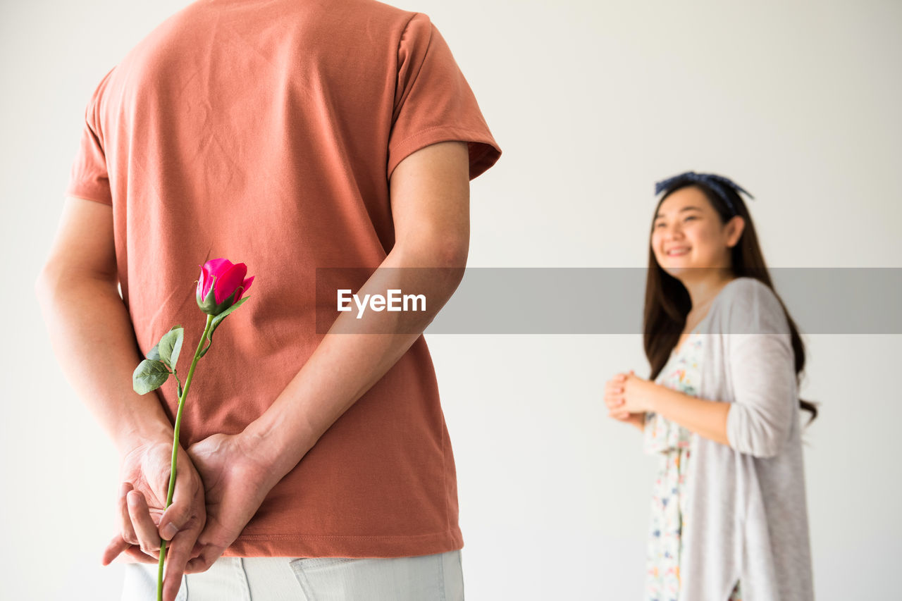 Young woman holding rose while standing against white wall