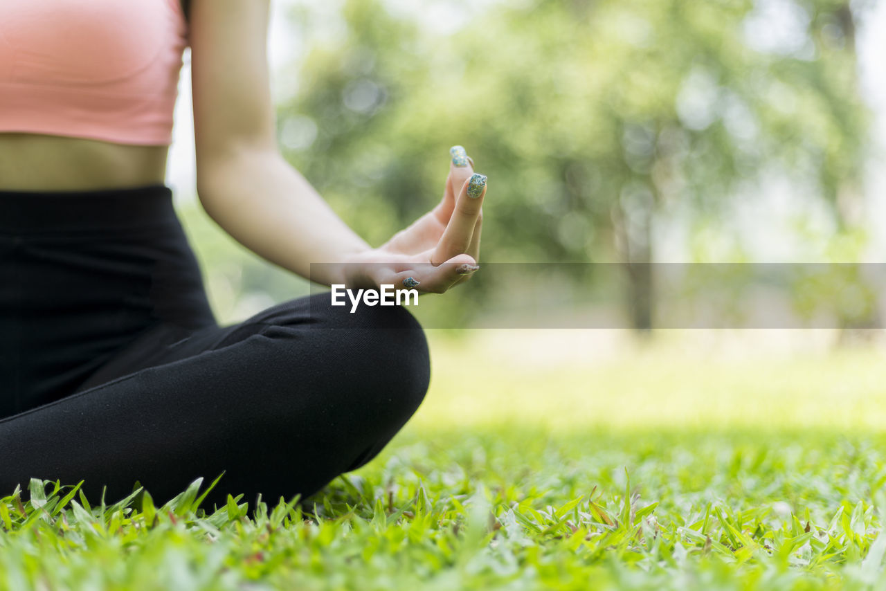 Midsection of woman meditating while sitting on grassy field at park