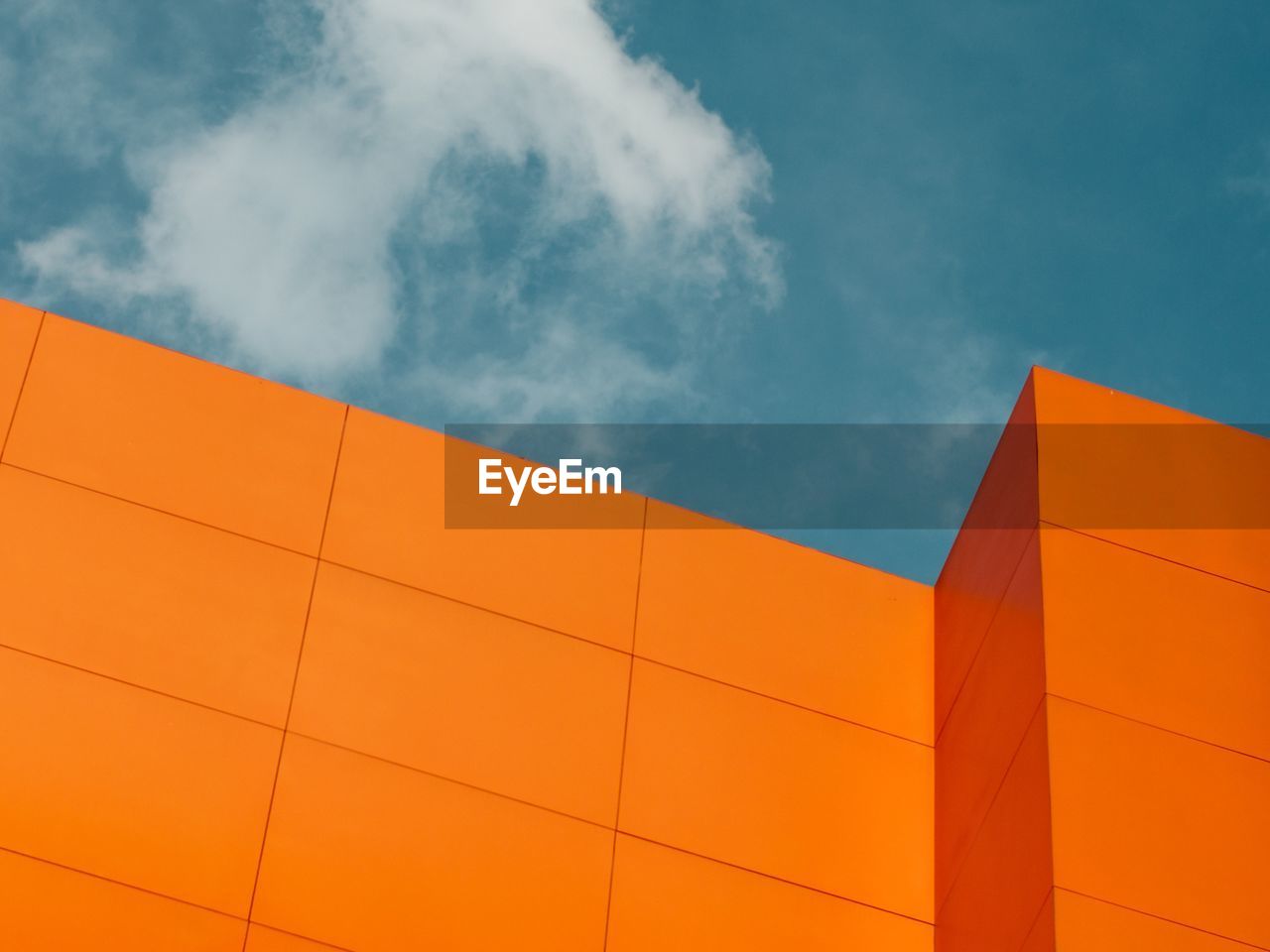 Low angle view of orange building against cloudy sky