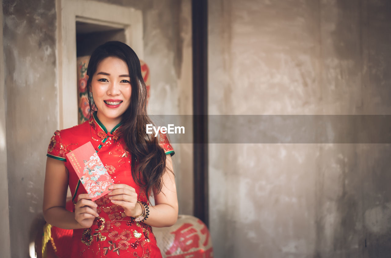 Portrait of beautiful young woman holding envelop standing against wall