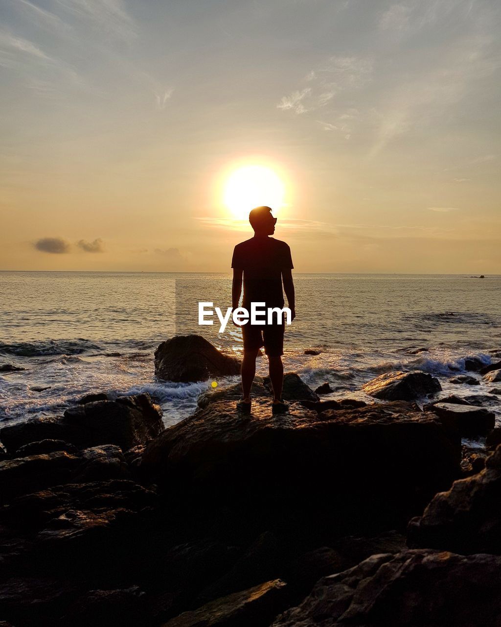 Full length of man standing on rock at beach during sunset