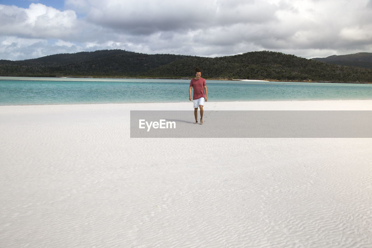 Tourist with a red shirt walking on white sandy australian beach