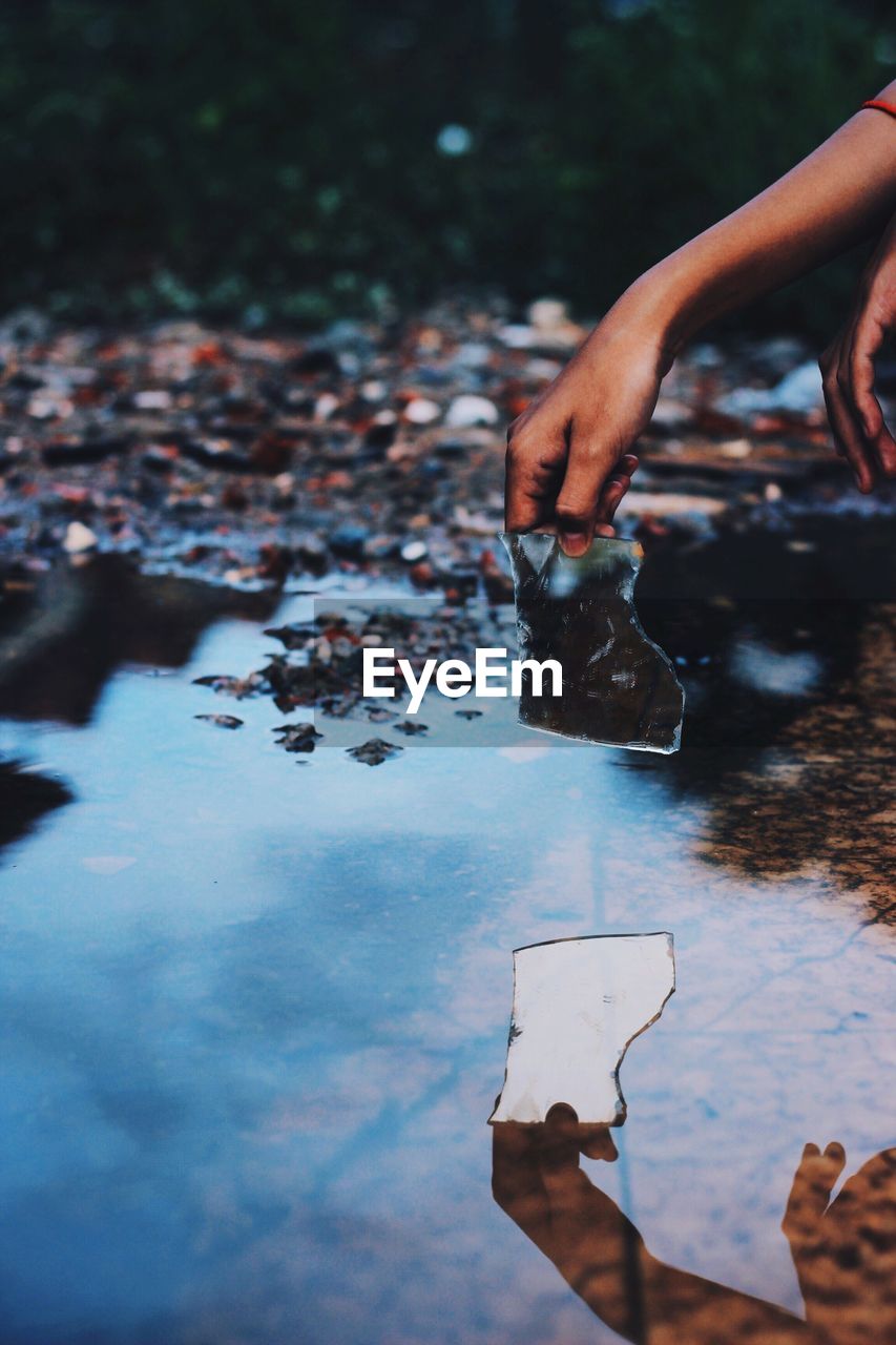 Reflection of cropped hand holding mirror on puddle