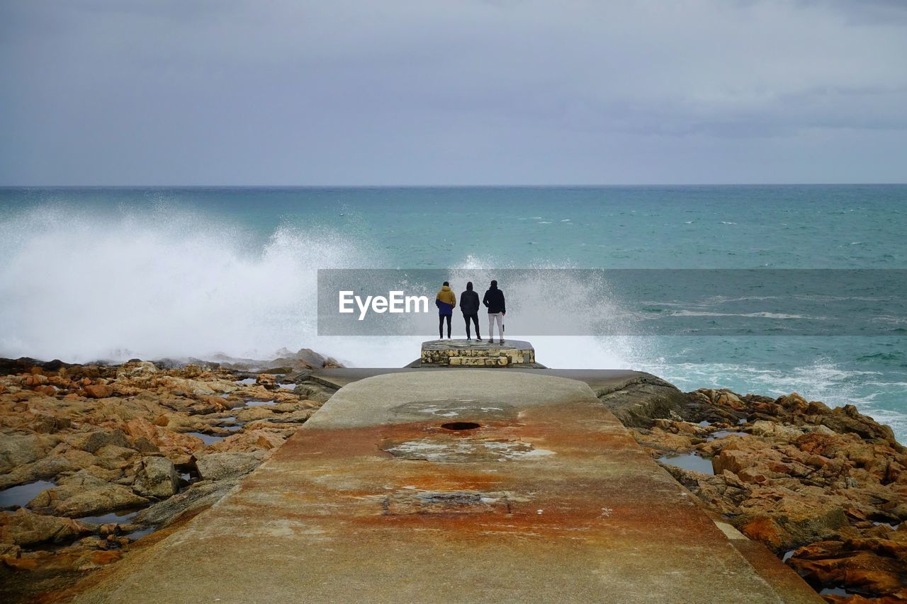 PANORAMIC VIEW OF MAN ON ROCK AGAINST SEA