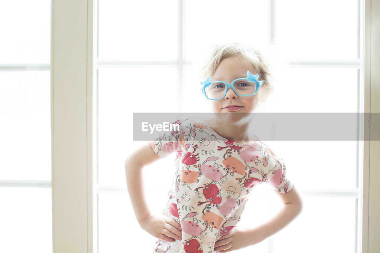 Portrait of girl wearing eyeglasses standing by window at home