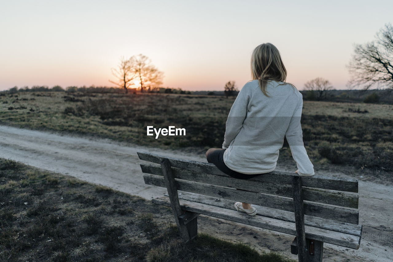 Rear view of woman looking at sunset while sitting on bench