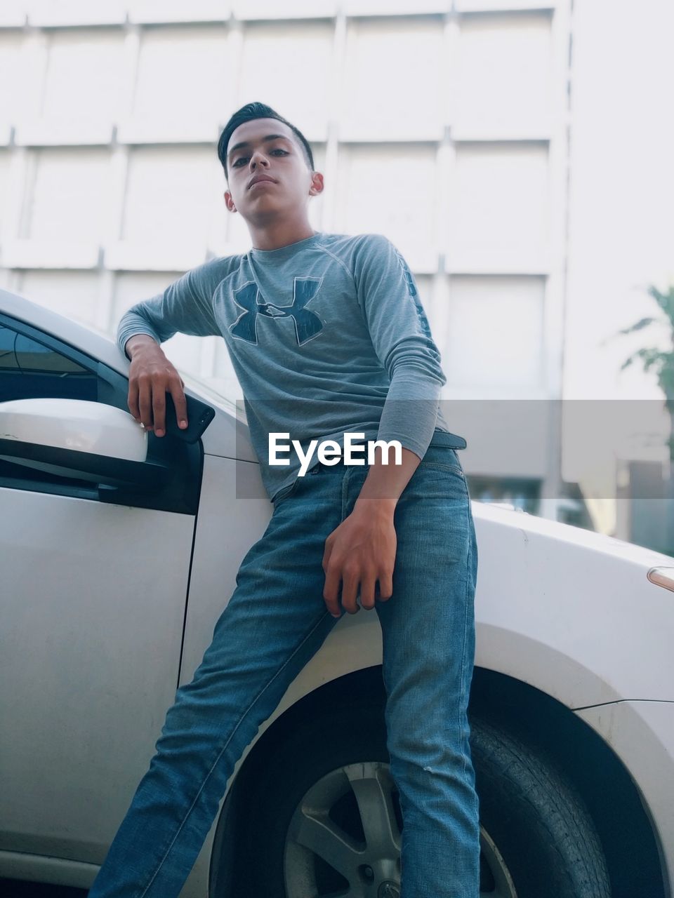 YOUNG MAN LOOKING AWAY WHILE SITTING ON CAR