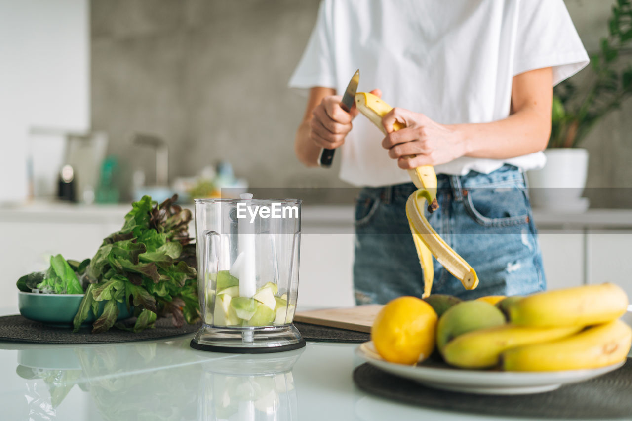 Young slim woman in white t-shirt and jeans cooking smoothie with bananas healthy food in kitchen 