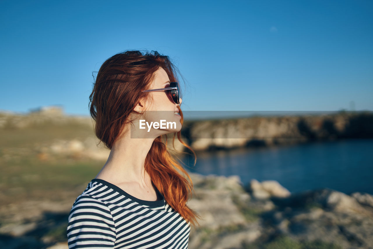 PORTRAIT OF YOUNG WOMAN WEARING SUNGLASSES STANDING OUTDOORS