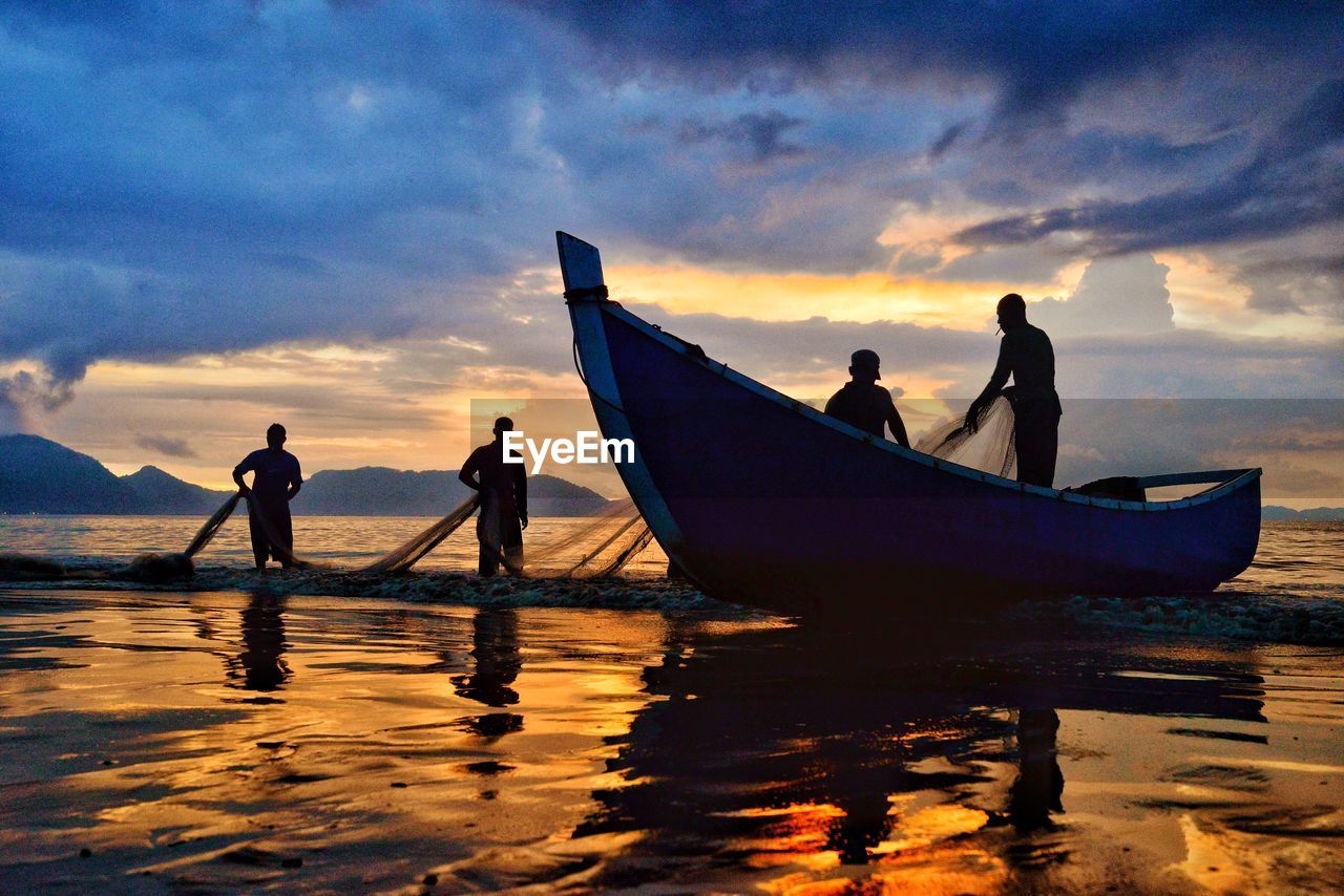 Silhouette people fishing in sea against sky during sunset