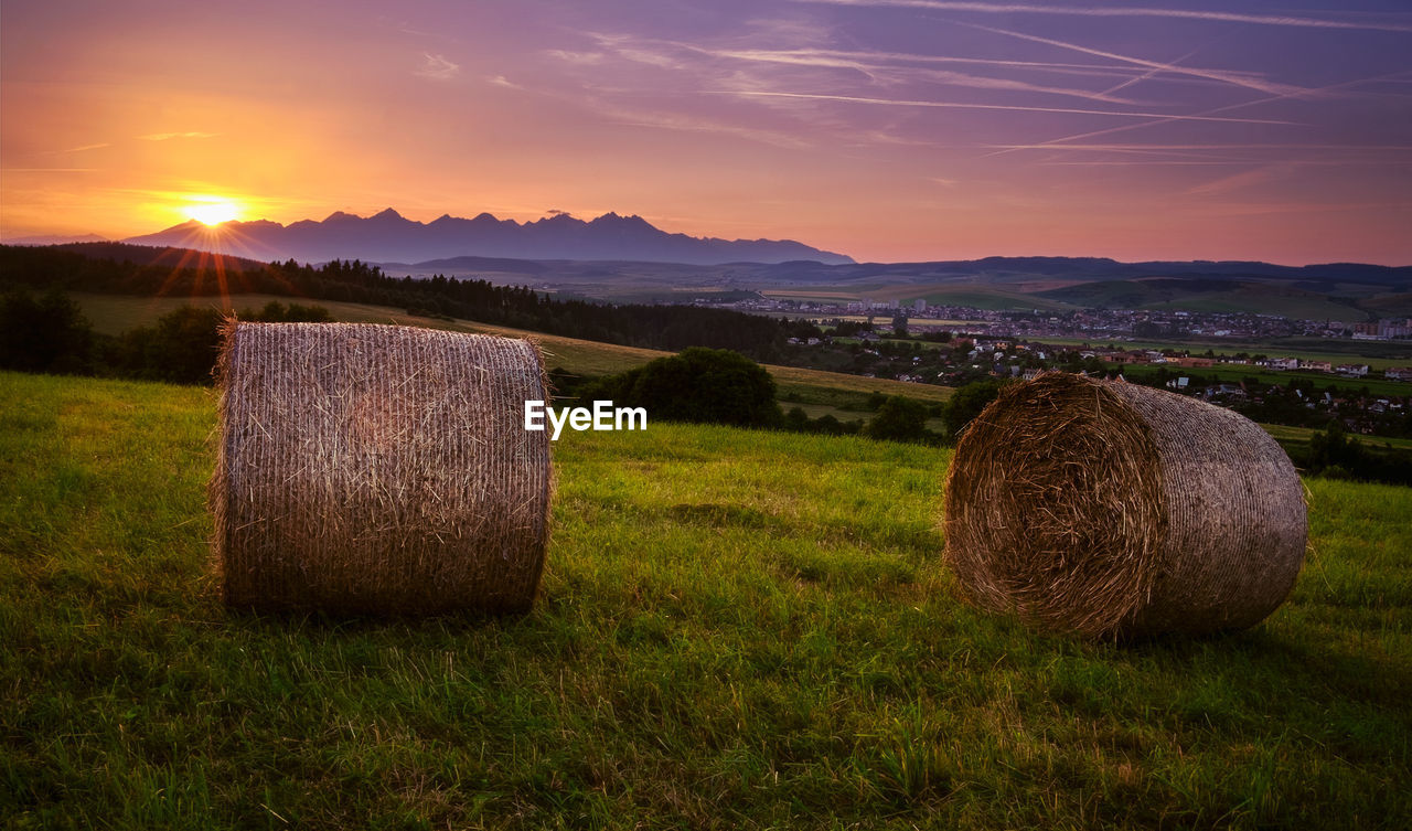 Hay bales on field against sky during sunset