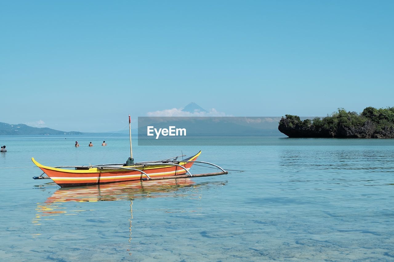 Boats moored on sea against clear blue sky