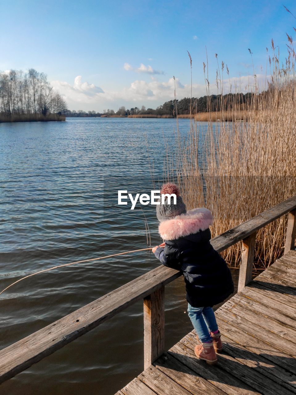 Side view of girl fishing in lake while standing by railing