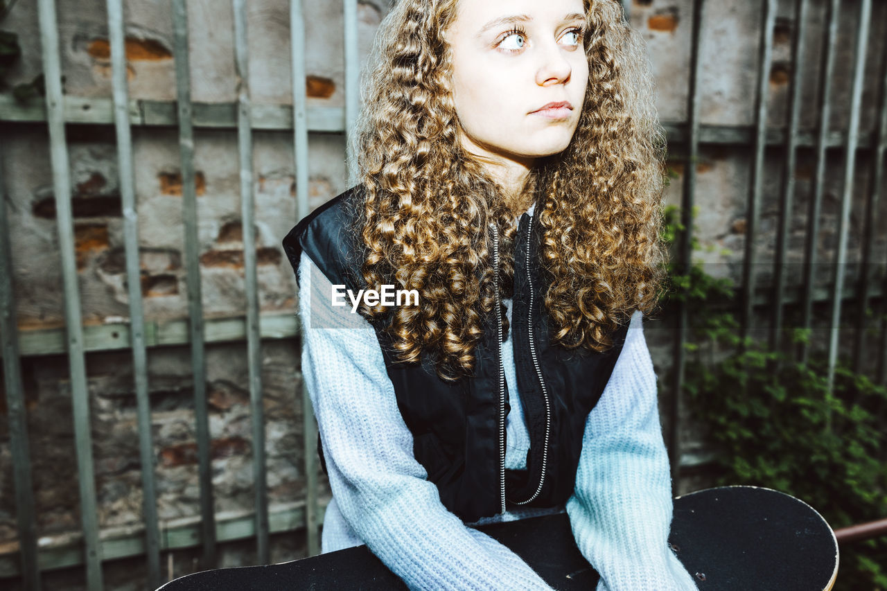 Contemplative girl with curly hair looking away against wall