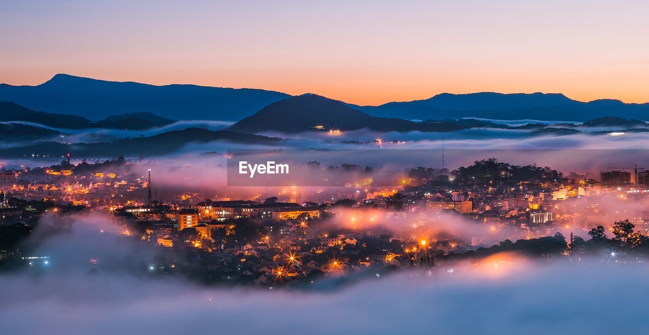 Illuminated city against sky during sunset