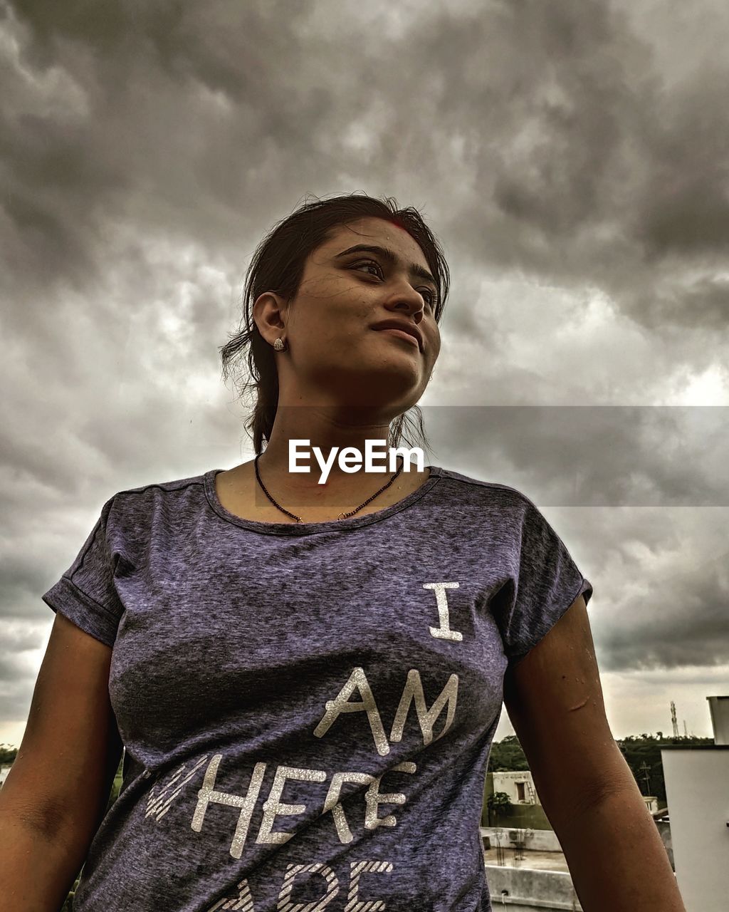LOW ANGLE PORTRAIT OF WOMAN STANDING AGAINST SKY