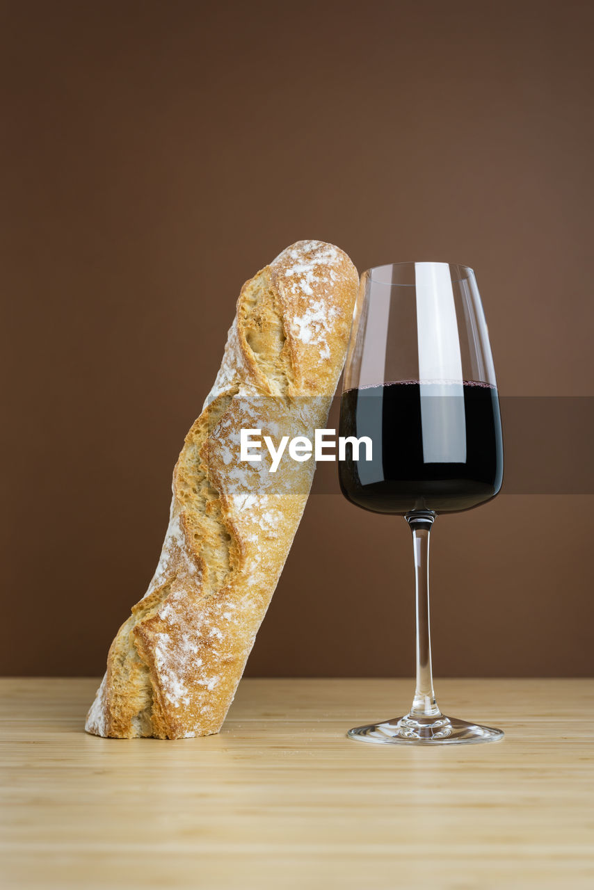 Minimalistic composition of a glass of red wine and a baguette.