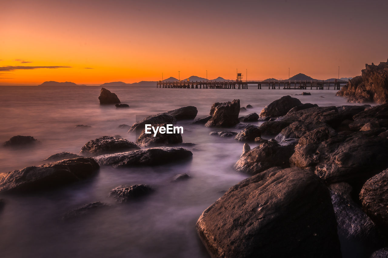 Rocks in sea against sky during sunset