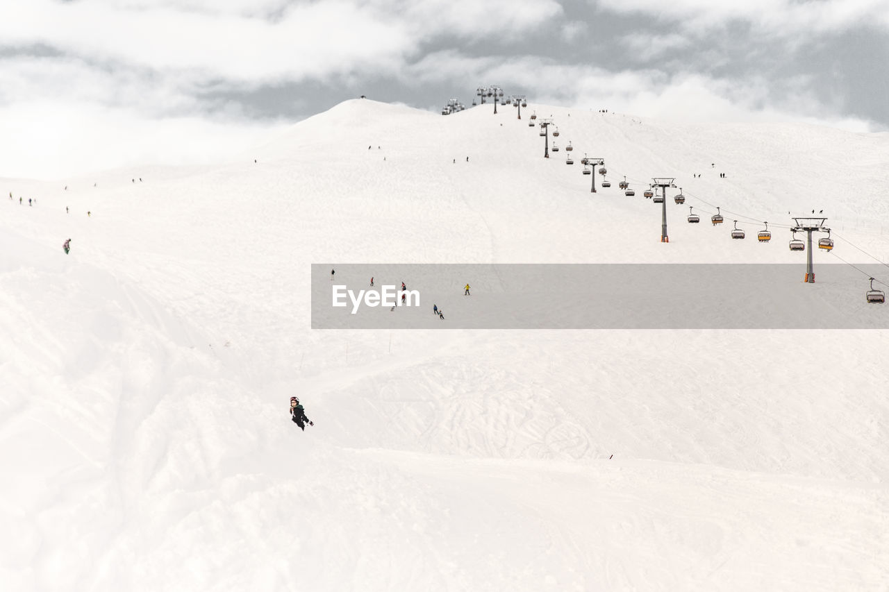 People skiing by ski lift on snowcapped mountains during sunny day