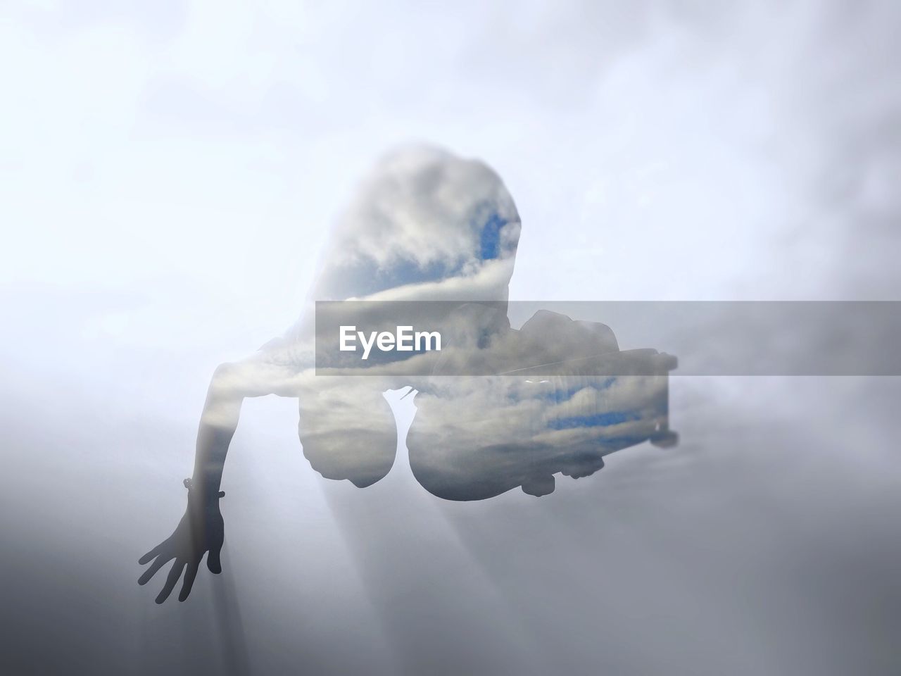 Double exposure of person jumping with skate board against cloudy sky