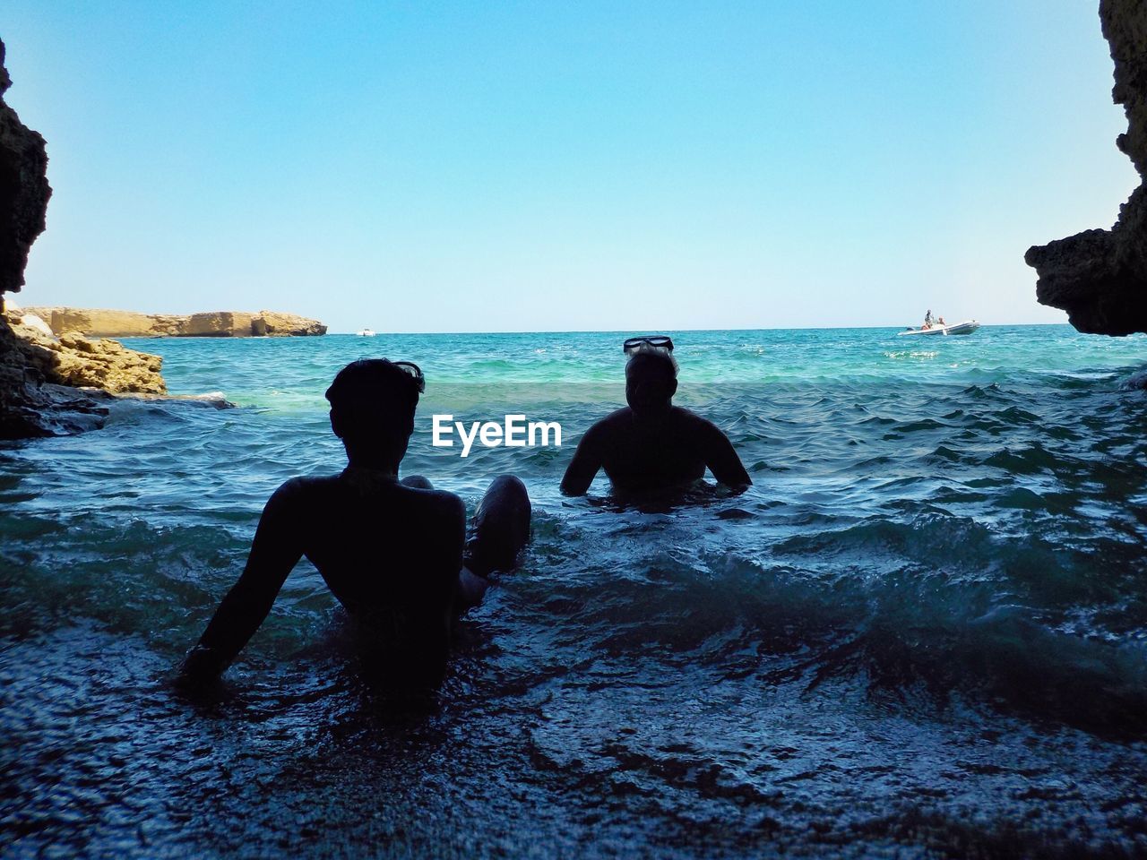 Silhouette male friends sitting on shore against blue sky