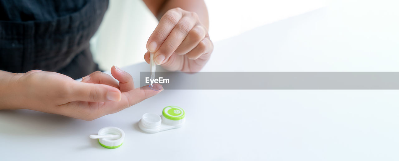 Girl puts contact lens on her index finger with tweezers.. close-up, side view, banner, copy space
