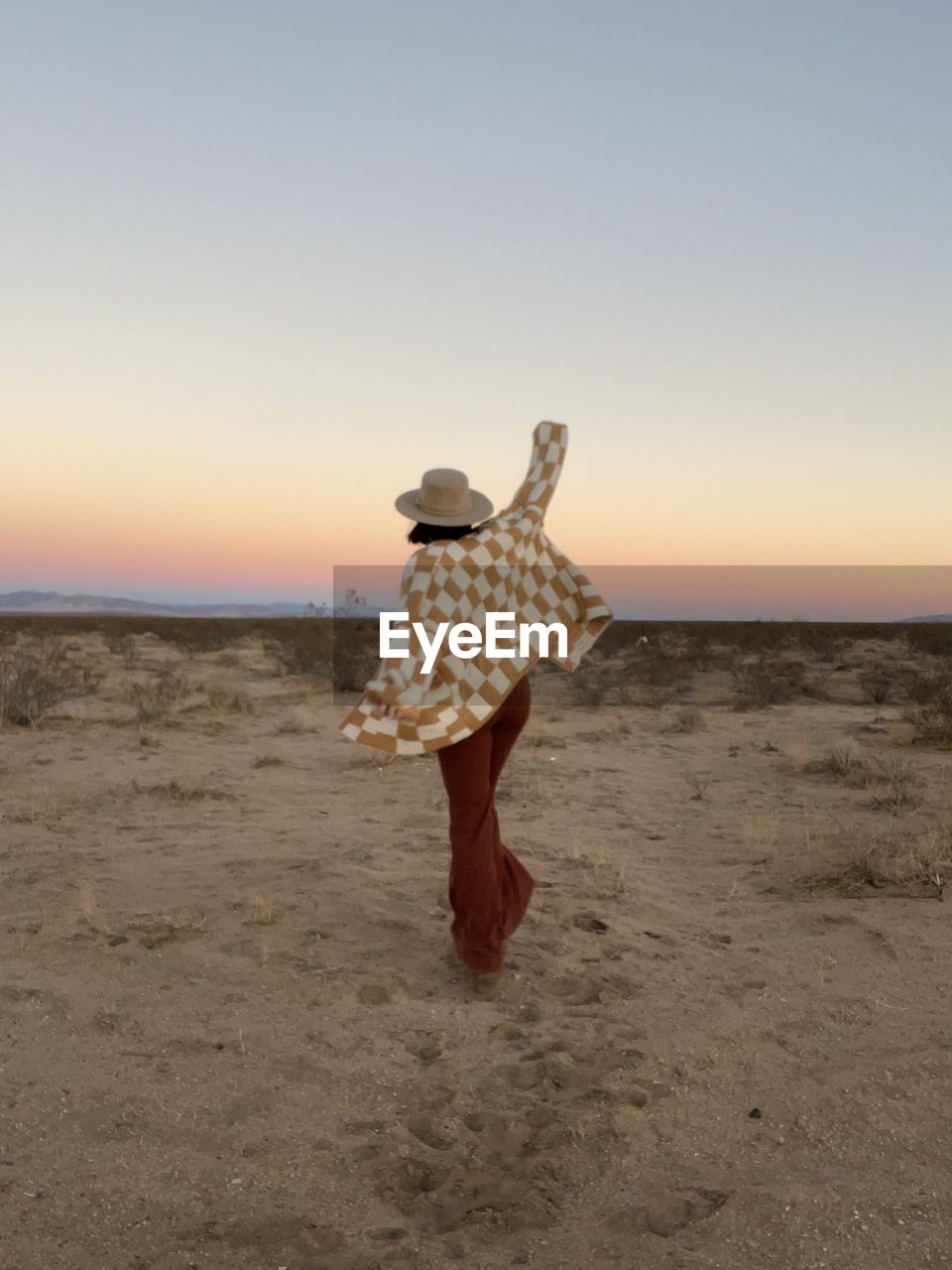 Girl in checkered sweater and hat dances at sunset in deser