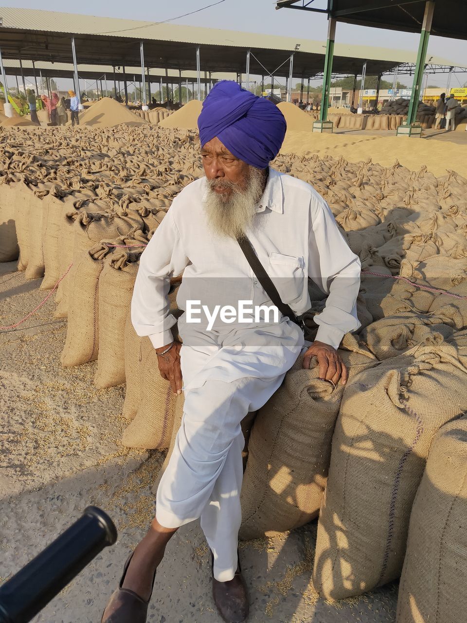 Mature man wearing turban sitting on sack at warehouse