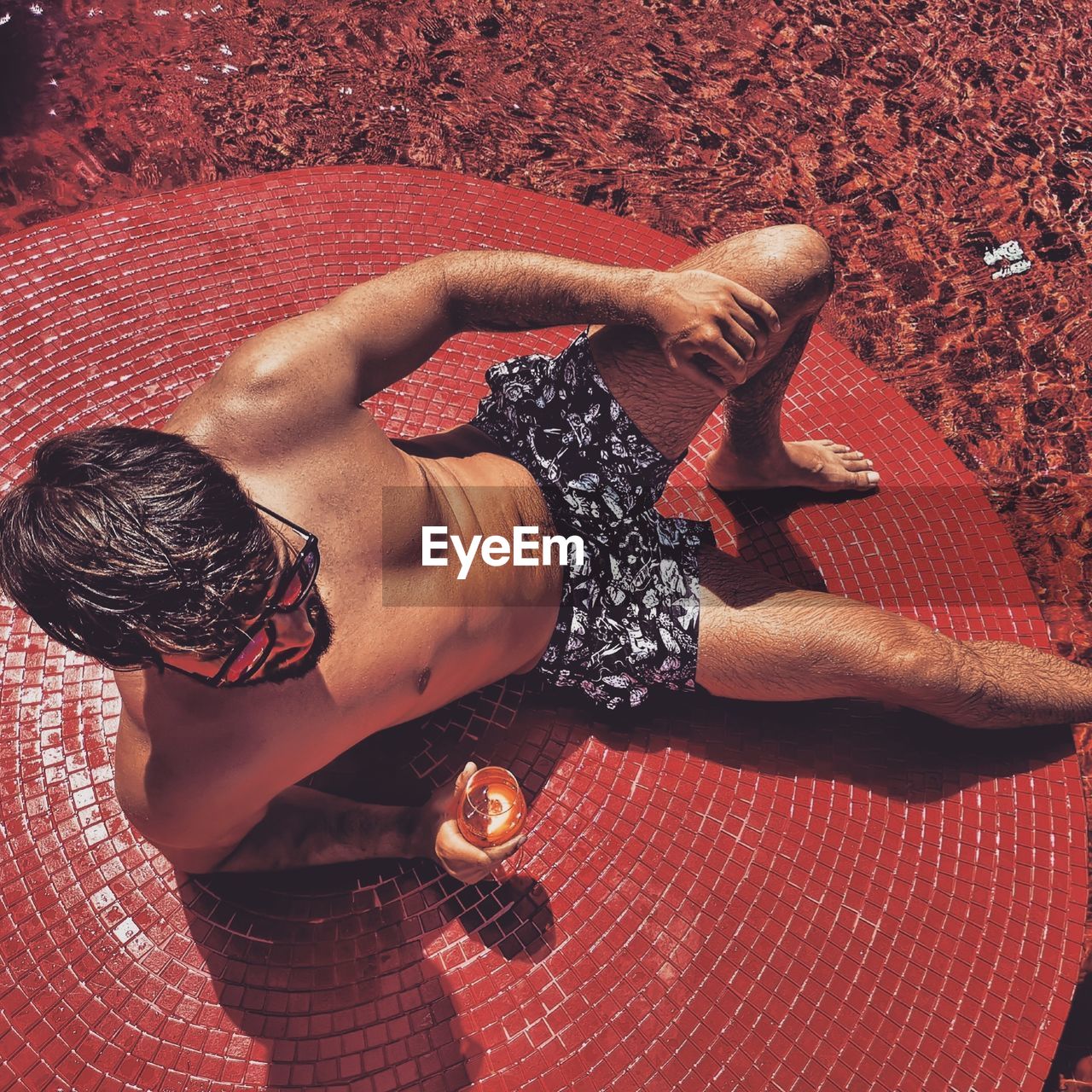 High angle view of shirtless man with alcohol sitting on tiled floor during sunny day