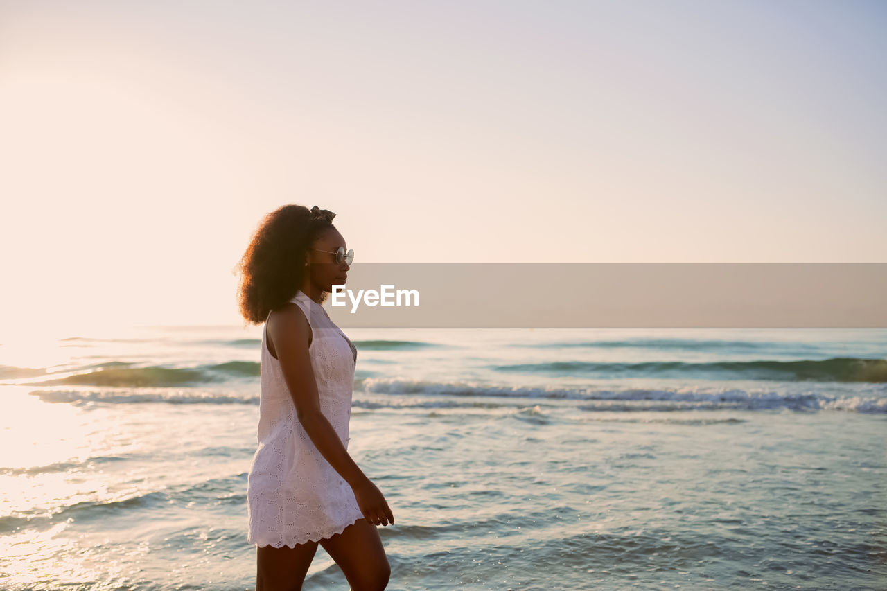 rear view of woman standing at beach against sky during sunset