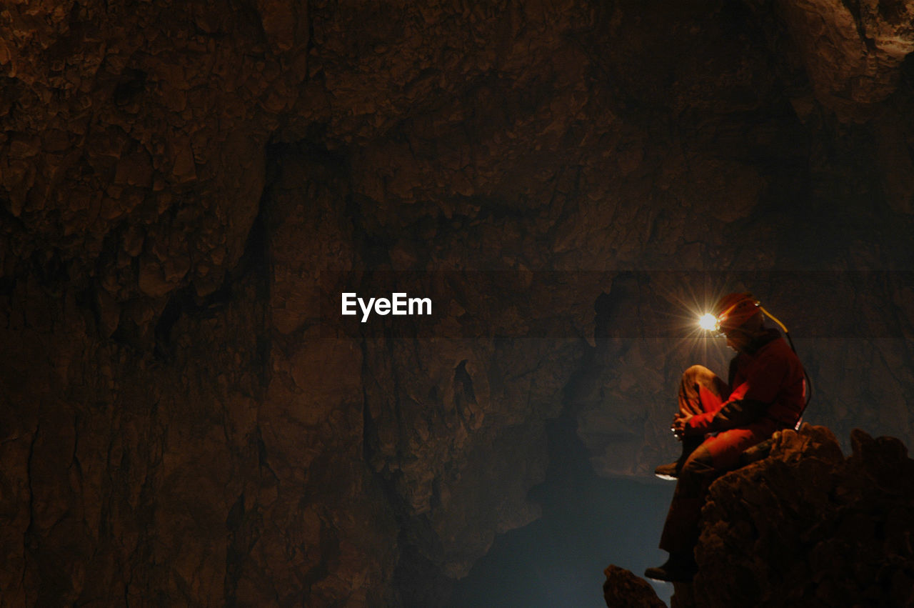 Side view of spelunker wearing illuminated headlamp in cave