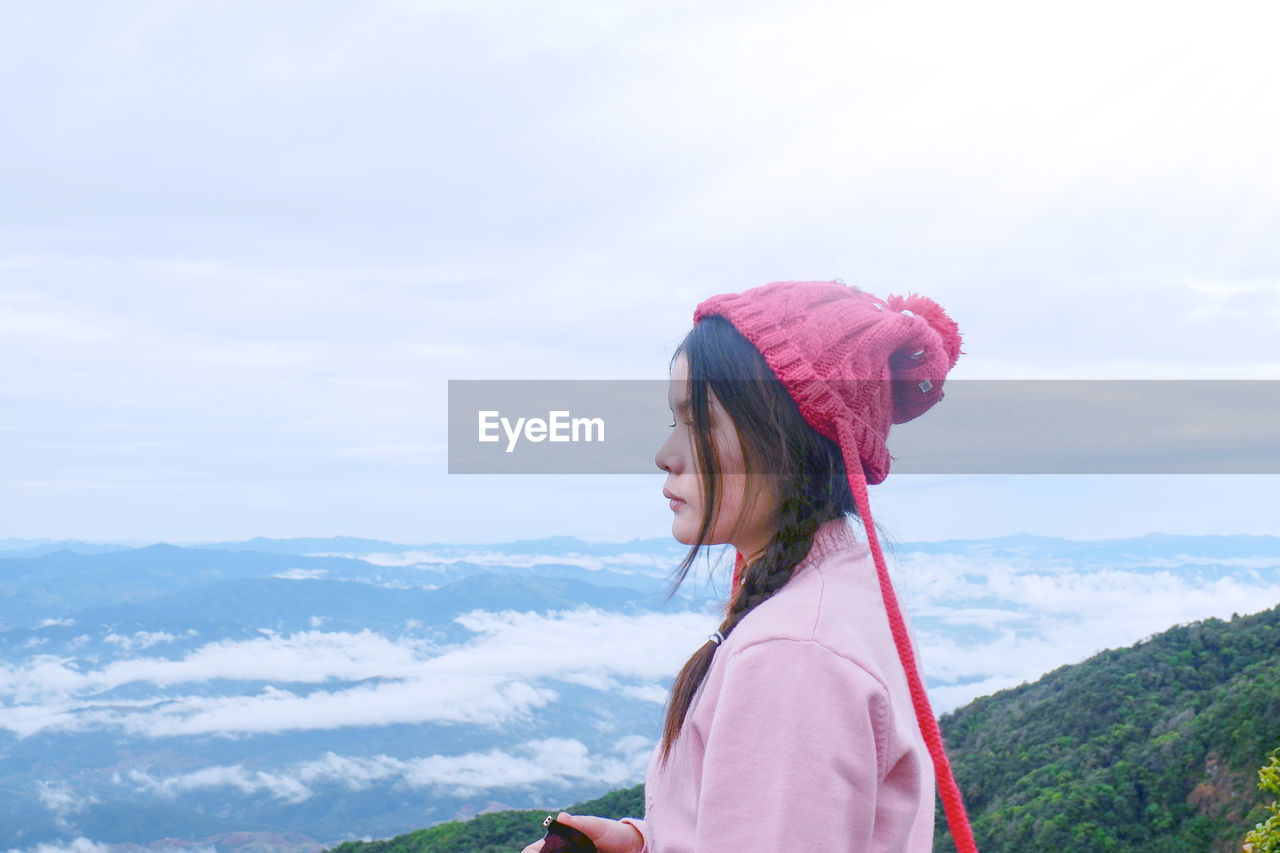 Side view of woman standing on mountain peak against cloudy sky