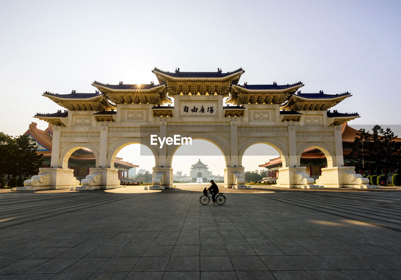 Person riding bicycle in front of gate against sky