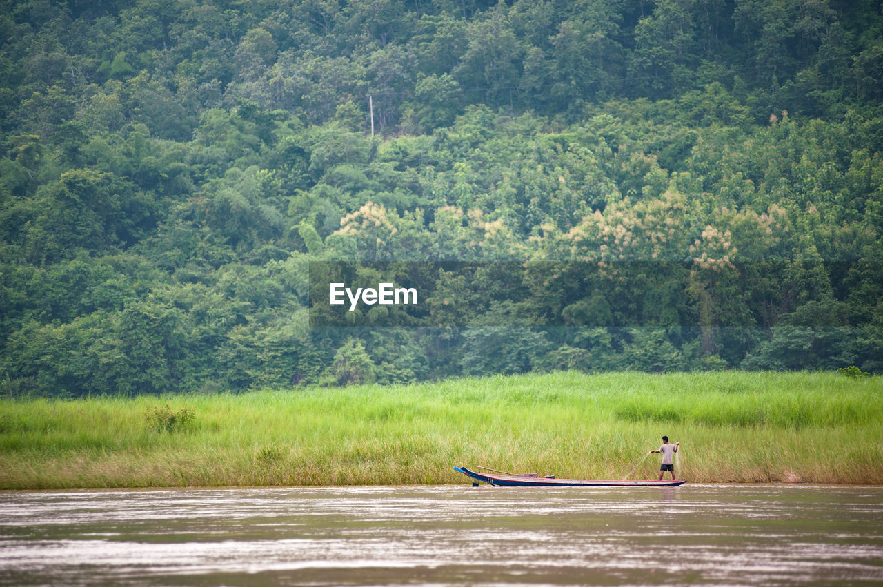 Distant view of fisherman fishing on river against forest