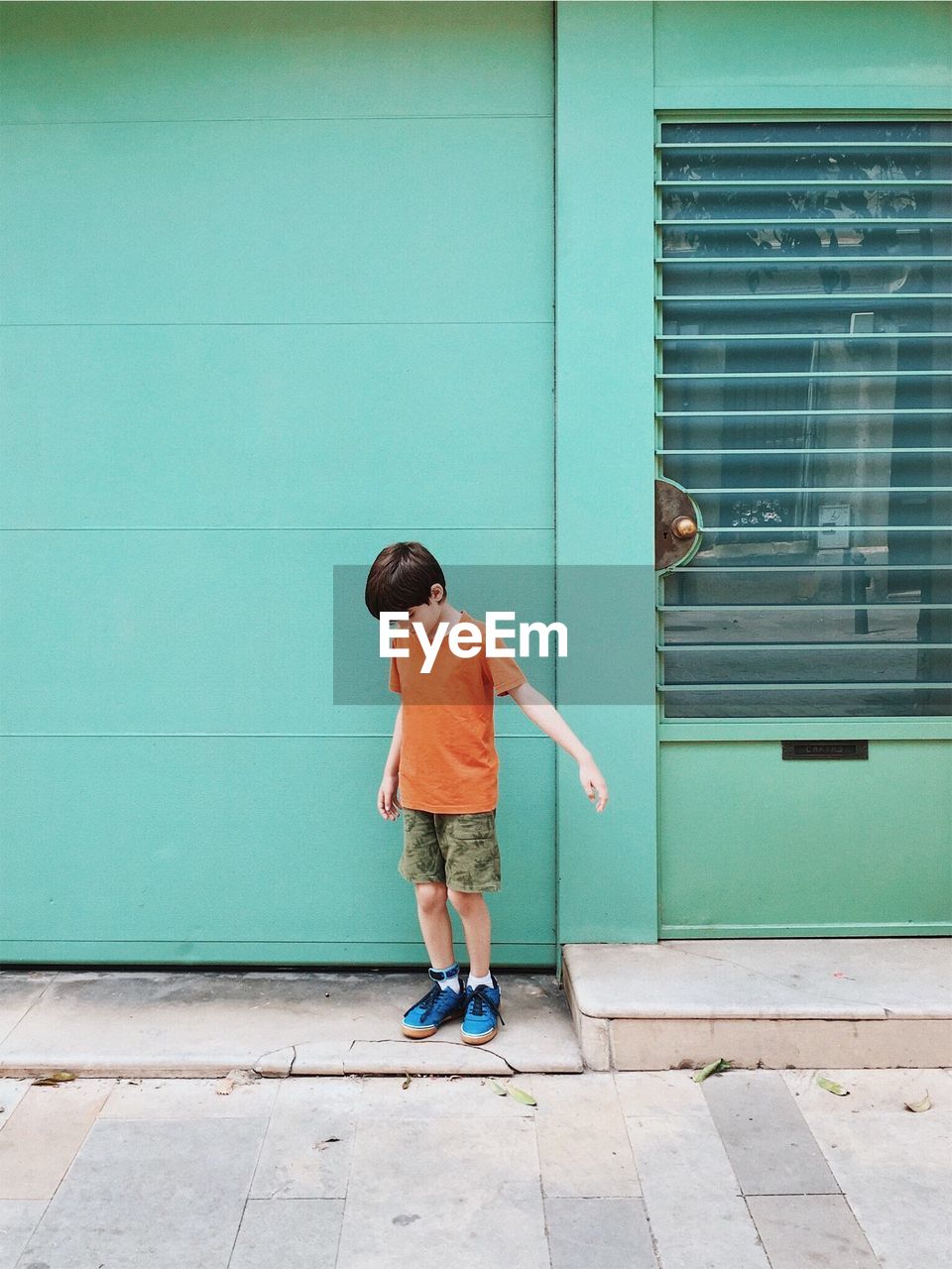 Full length of boy standing on footpath against building 