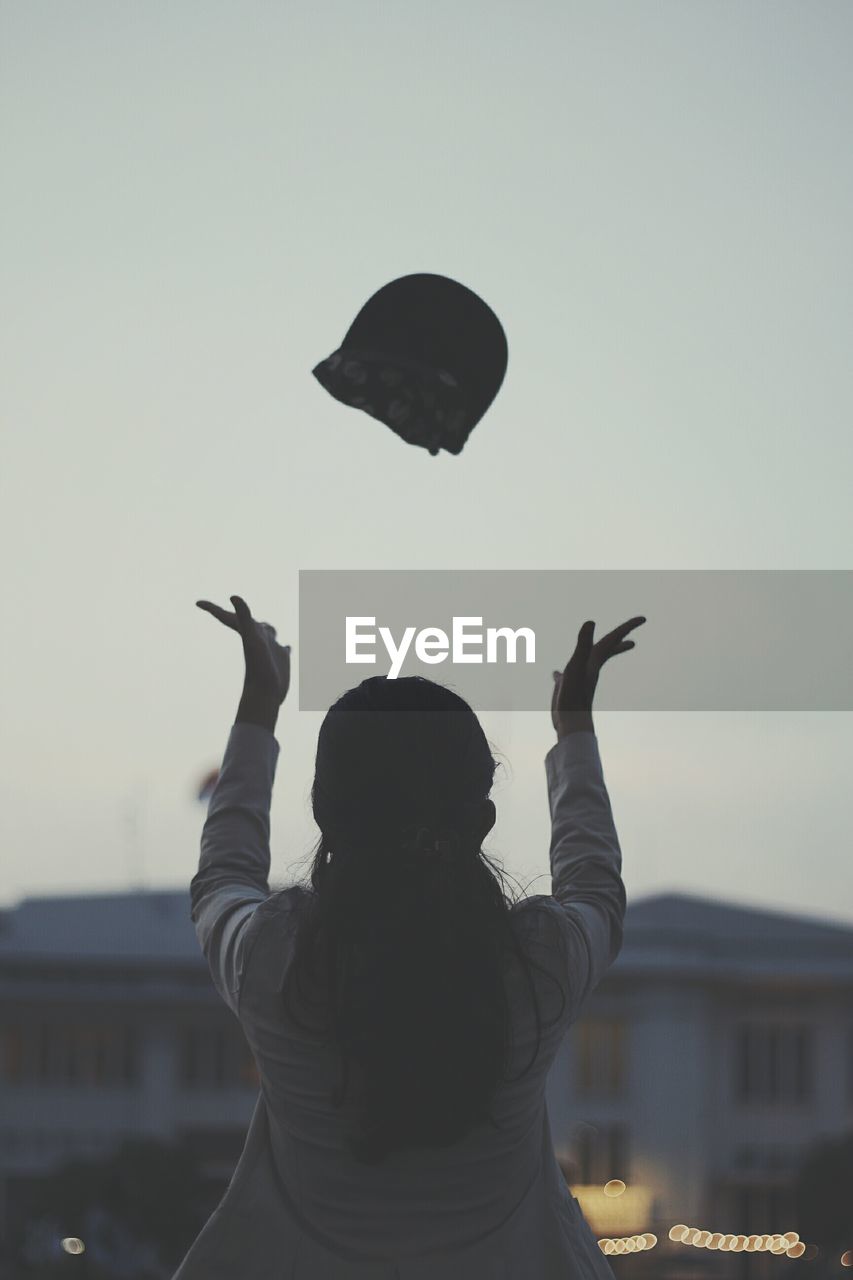 Rear view of woman throwing cap against clear sky