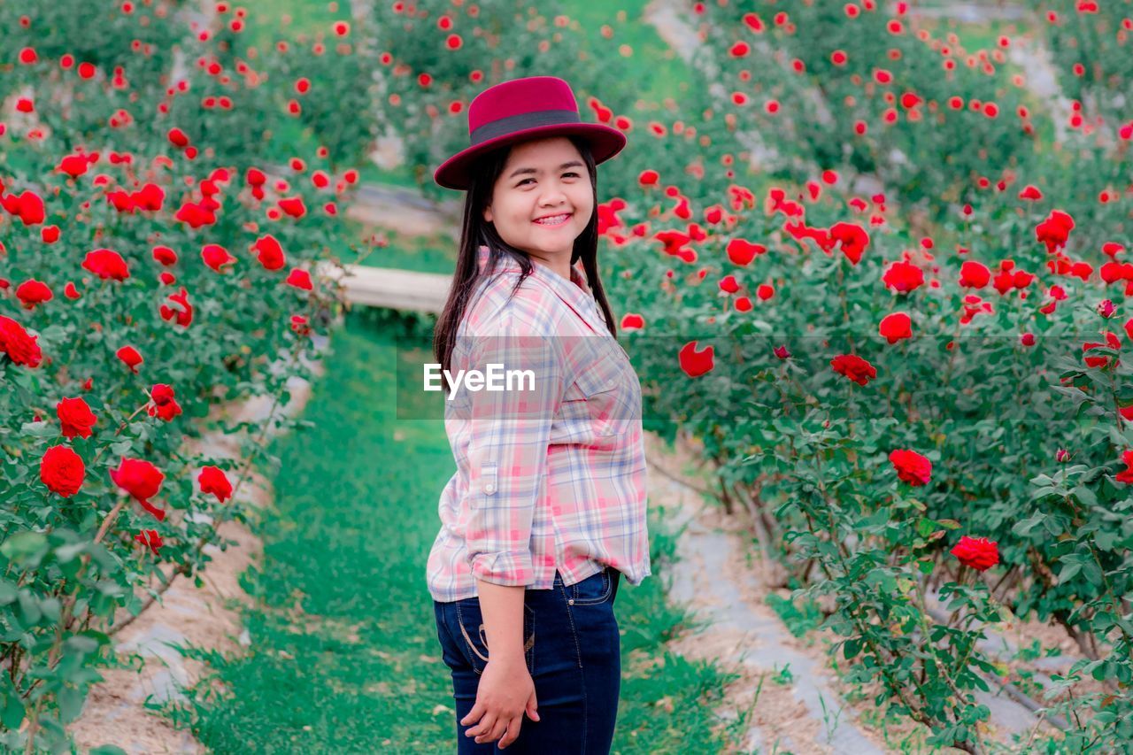 Portrait of smiling woman standing by red flowering plants