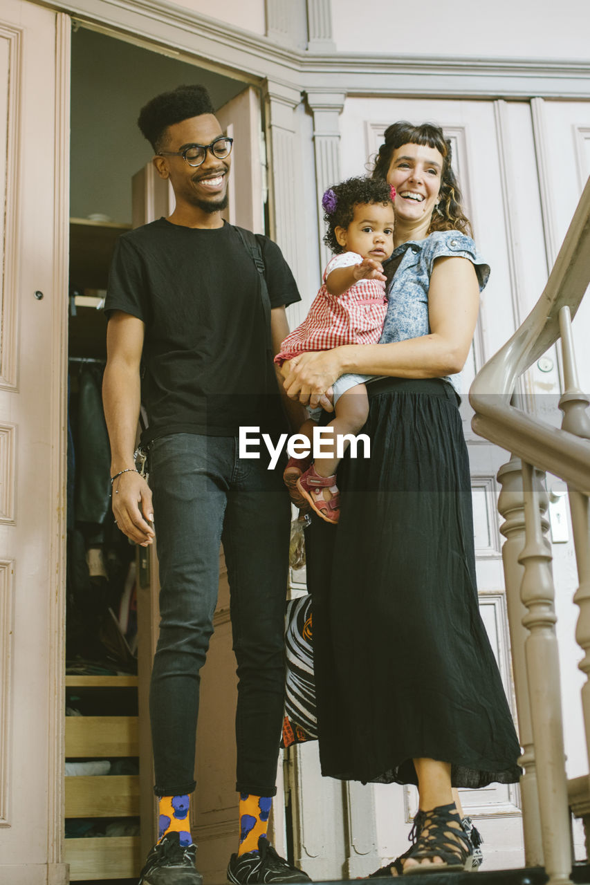 Happy mother and father with daughter at entrance in apartment