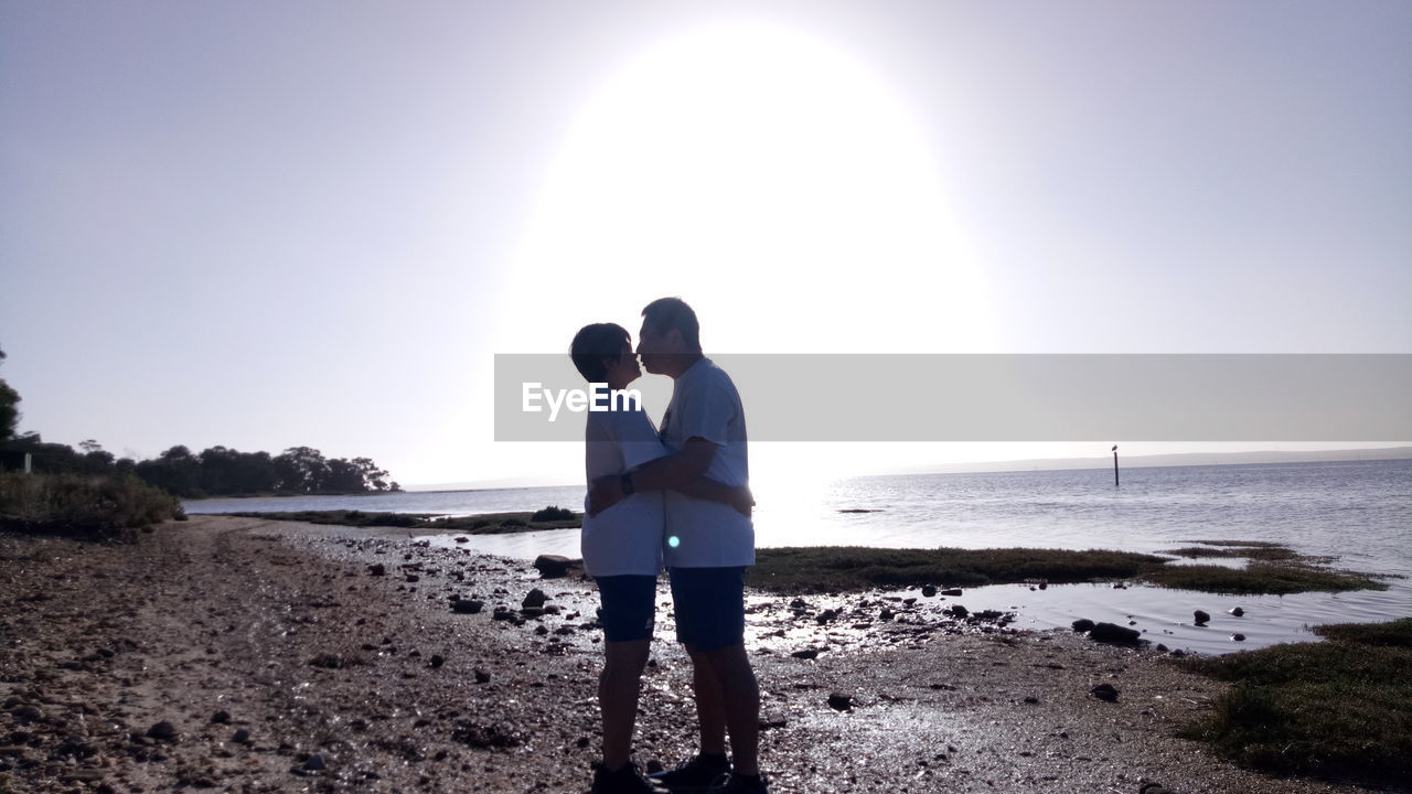 Couple kissing while standing at beach against clear sky