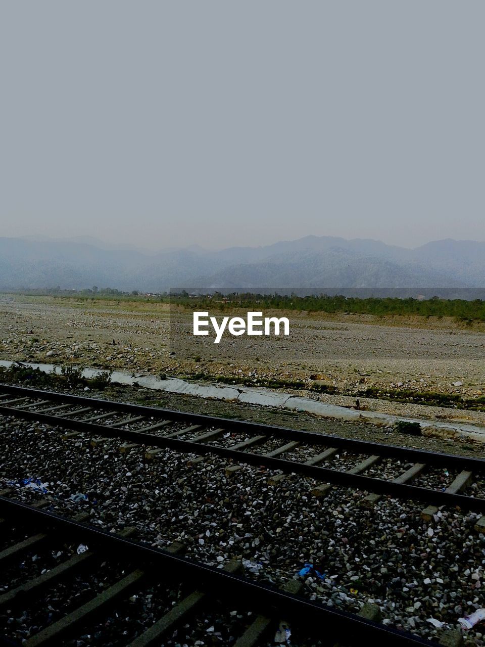 Railroad tracks by field against sky during foggy weather