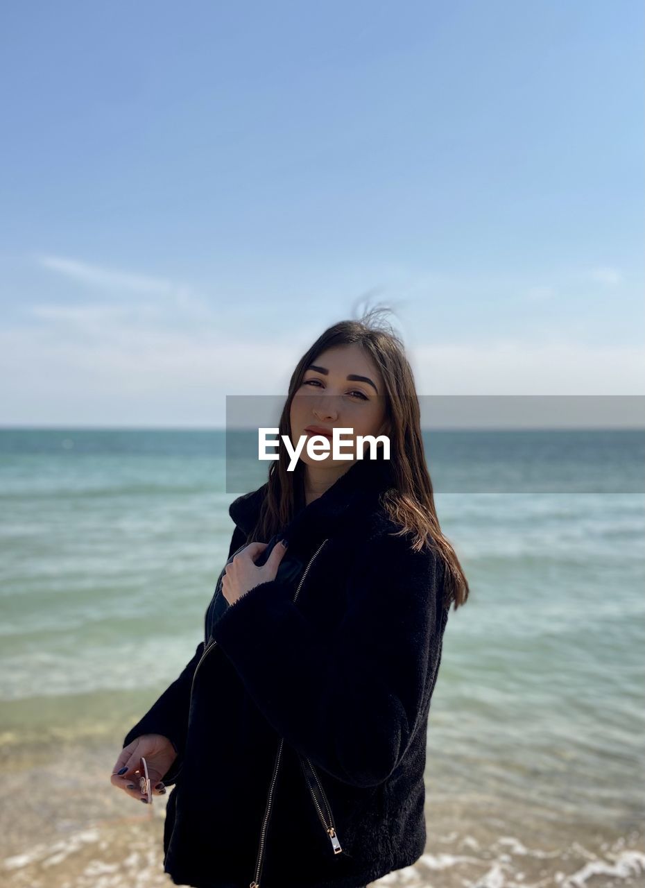 YOUNG WOMAN STANDING ON BEACH AGAINST SKY