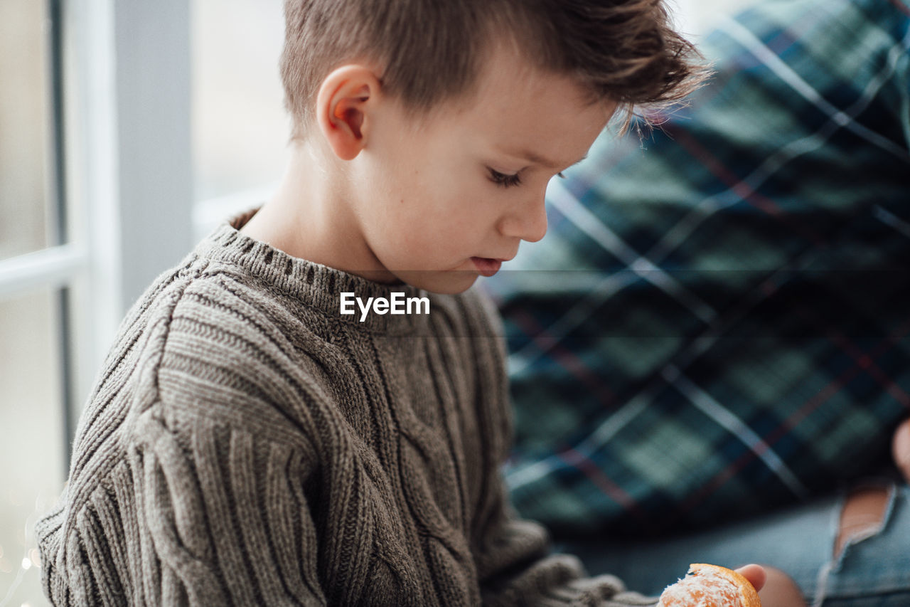 Side view of boy eating orange while sitting at home