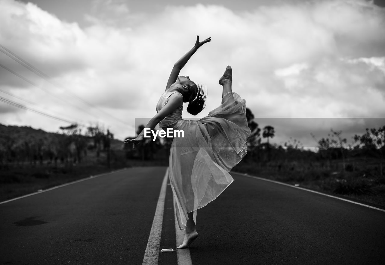 Young woman dancing on road against sky