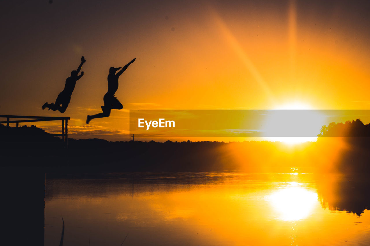 SILHOUETTE OF JUMPING OVER LAKE AGAINST SUNSET SKY