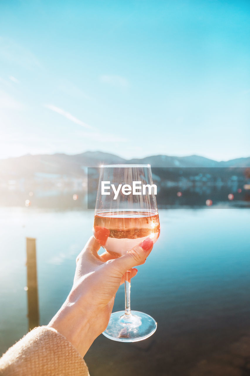 Female hand with glass of rose wine. cozy pier on the coast of lake tegernsee. mountains in bavaria