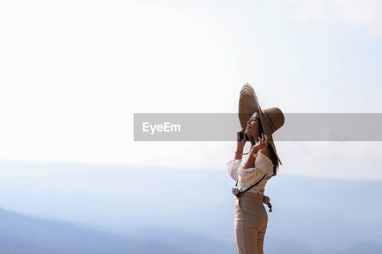 Side view of smiling woman wearing hat by mountains against sky