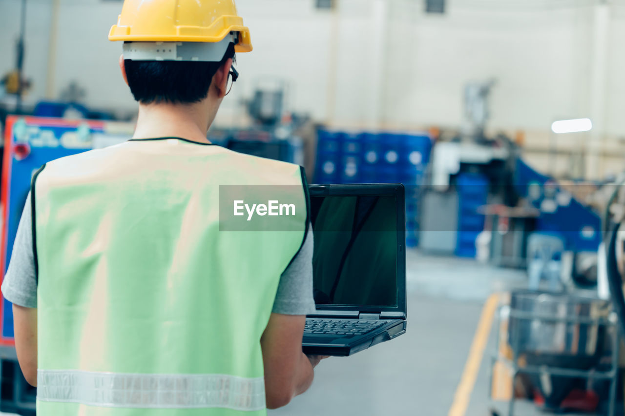 Rear view of man working while standing in factory