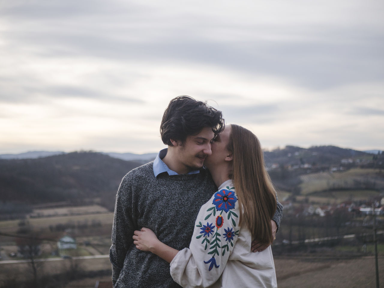 Woman kissing man against sky