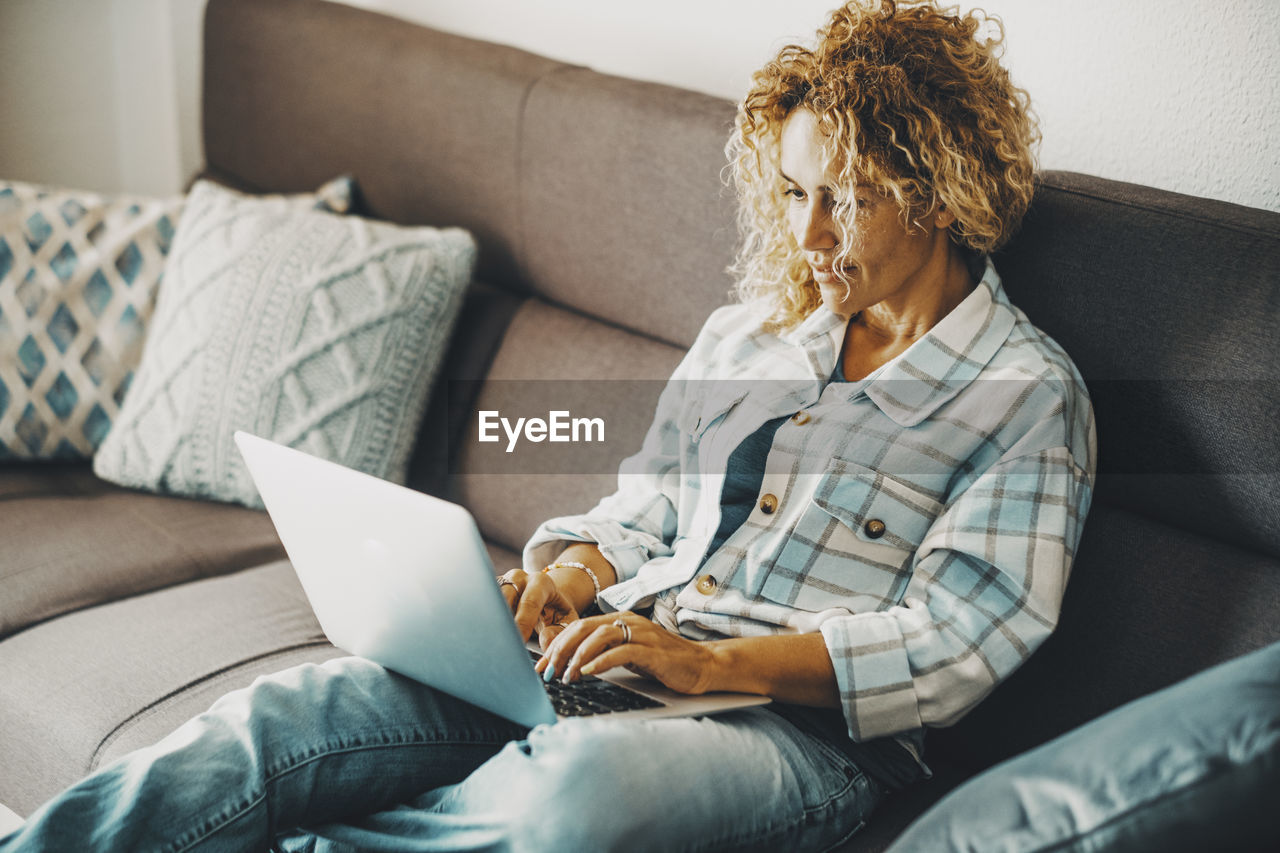 young woman using mobile phone while sitting on sofa at home